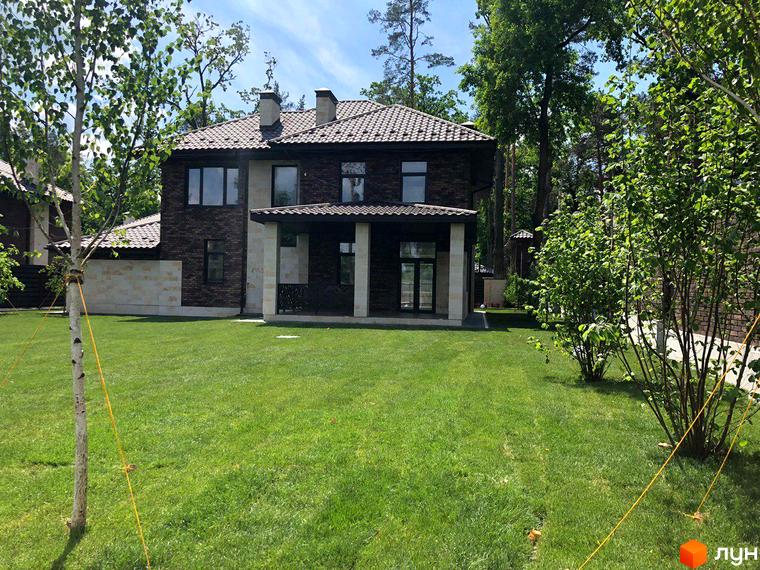 Котеджне містечко Zahrava Village: двоповерховий будинок з коричневої цегли та світлими колонами, зелений газон та дерева навколо.