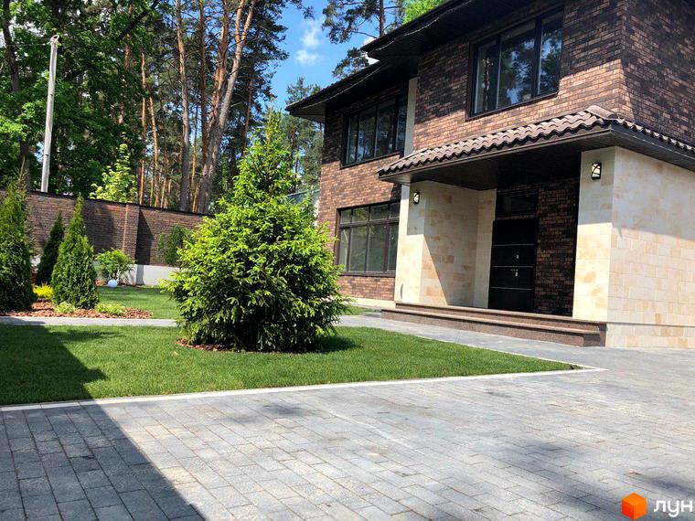 Котеджне містечко КМ Zahrava Village: двоповерховий будинок з коричневої цегли та світлого каменю, зелений газон та бруківка перед будинком.