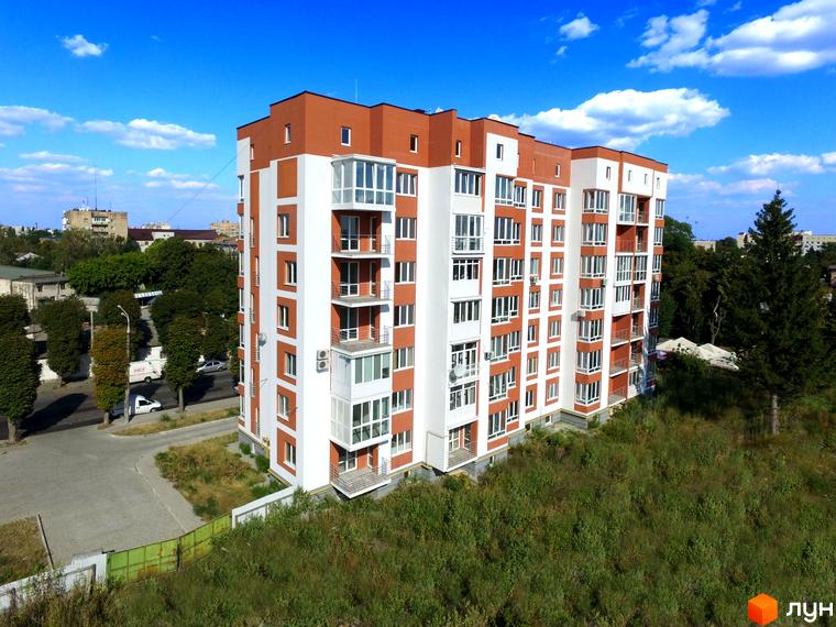 Багатоповерховий будинок ЖК Сіті Парк з білими та коричневими фасадами. Навколо будинку зелень та блакитне небо з хмарами.