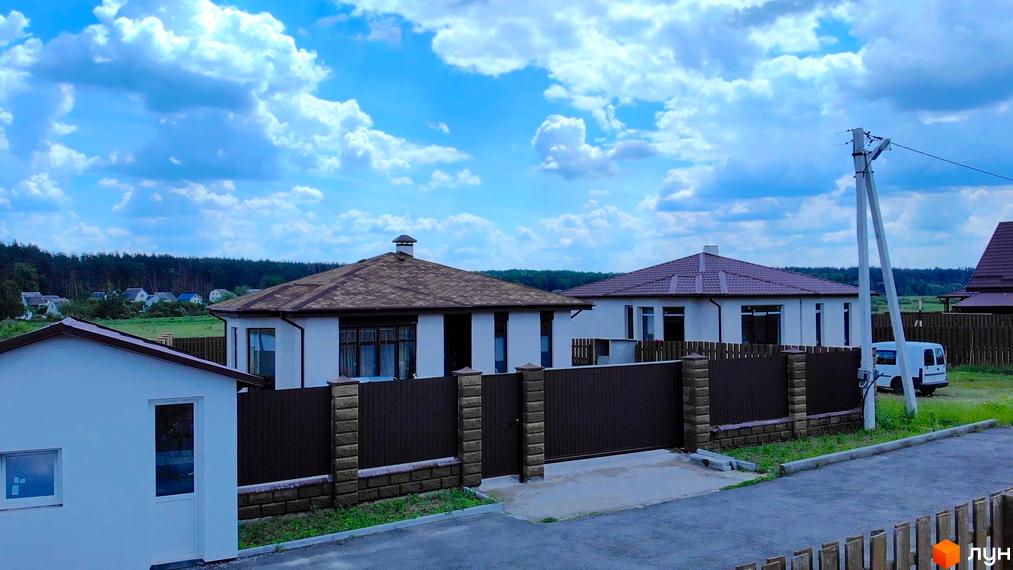 Котеджне містечко Михайлівський хутір: білі будинки з коричневими дахами та парканом. На території новобудови є парковка для білого фургона.