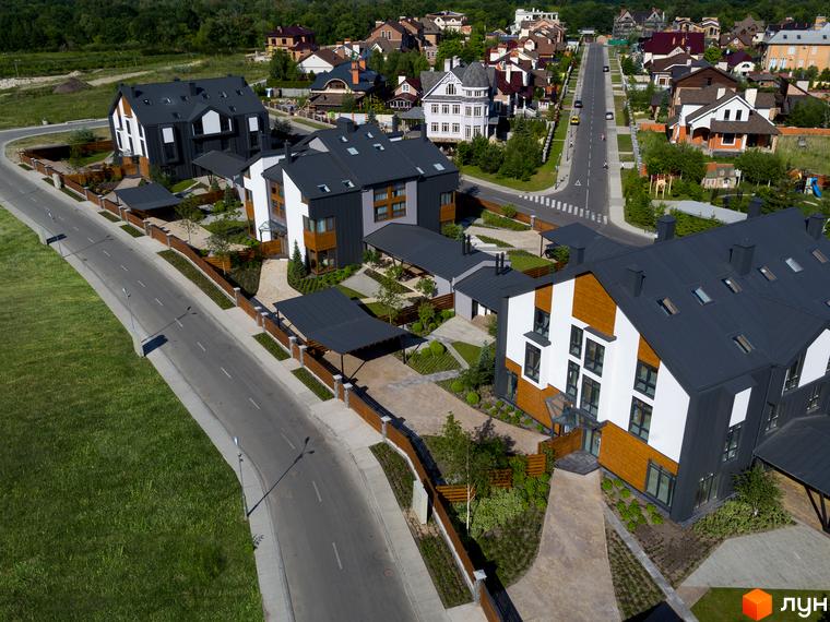 Таунхауси в ЖК. Будинки з темними дахами та оздобленням деревом. Доглянута прибудинкова територія з газонами та алеями.