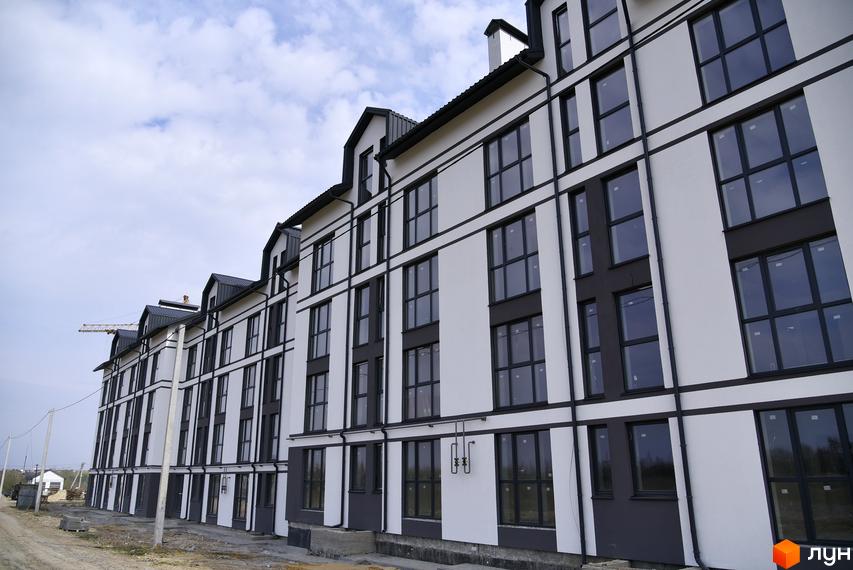 Фасад житлового комплексу Юпітер з великими вікнами та контрастним оздобленням. Навколо будинку видно будівельний майданчик та елементи інфраструктури.