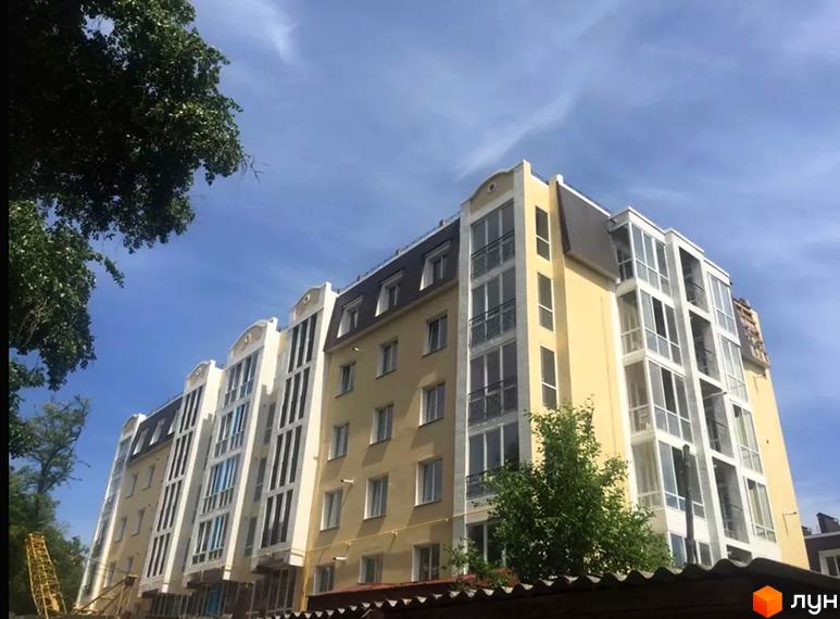 Зовнішній вигляд житлового комплексу на вул. Князя Чорного, 4а, з фасадами світло-жовтого та білого кольорів, великими вікнами та балконами. Навколо будівлі зелені дерева та блакитне небо.