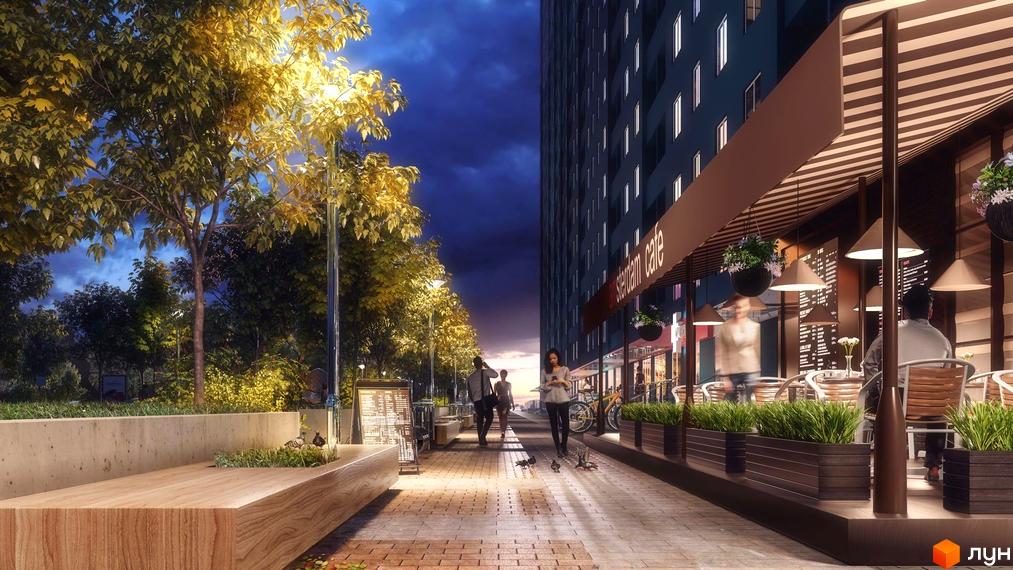 Житловий комплекс Одеський бульвар ввечері: висока будівля з освітленими вікнами та кафе на першому поверсі. Пішохідна алея з деревами, вуличними ліхтарями та лавками.
