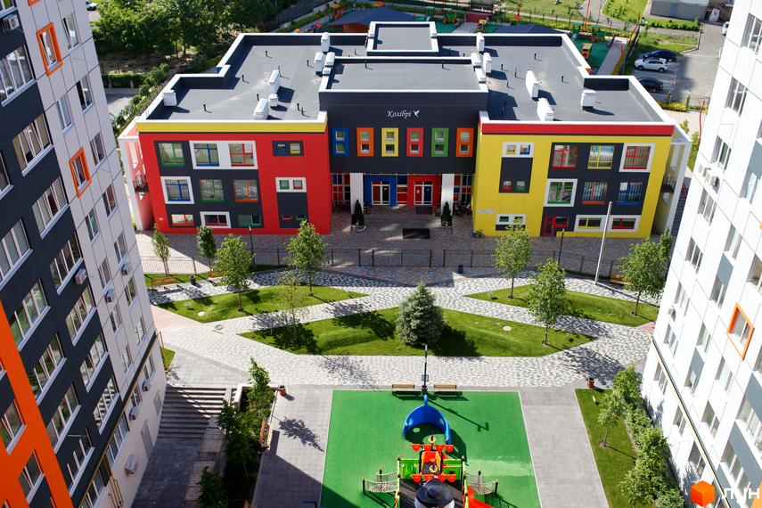 Житловий комплекс Синергія-3: яскрава будівля з кольоровими фасадами та вікнами, оточена зеленими насадженнями та дитячим майданчиком.