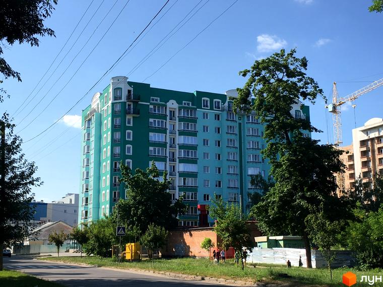 Зовнішній вигляд новобудови Павленківська площа, 3б, з яскраво-бірюзовим фасадом та білими вікнами. Навколо будинку зелені дерева та доглянута прибудинкова територія.