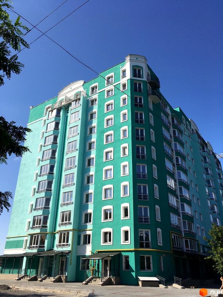 Яскравий зелений житловий комплекс Павленківська площа, 3б. Будинок має багато вікон та балконів, виходить на блакитне небо.