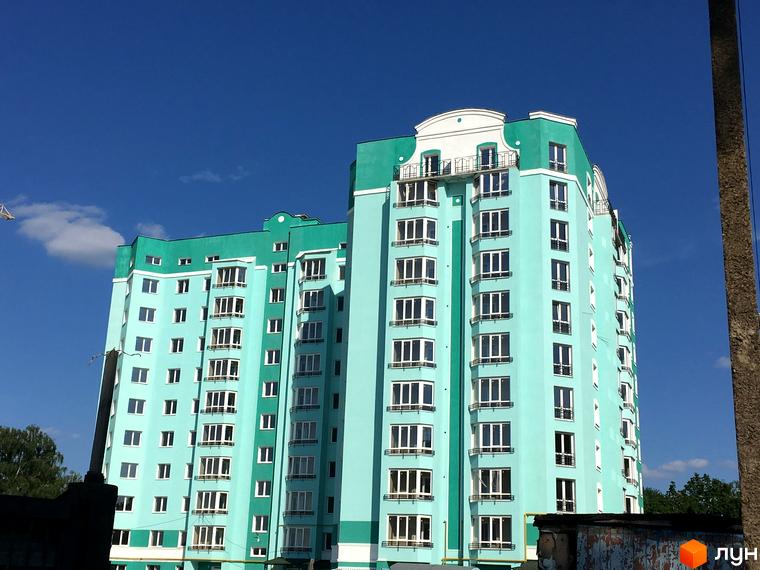 Зовнішній вигляд новобудови Павленківська площа, 3б, з багатоповерховими секціями блакитного кольору та балконами. Навколо будинку видно зелені насадження та елементи міської забудови.