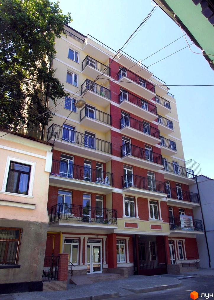 Багатоповерховий будинок ЖК На Каретном з балконами та великими вікнами. На першому поверсі розташовані вхідні групи з дверима та вікнами.