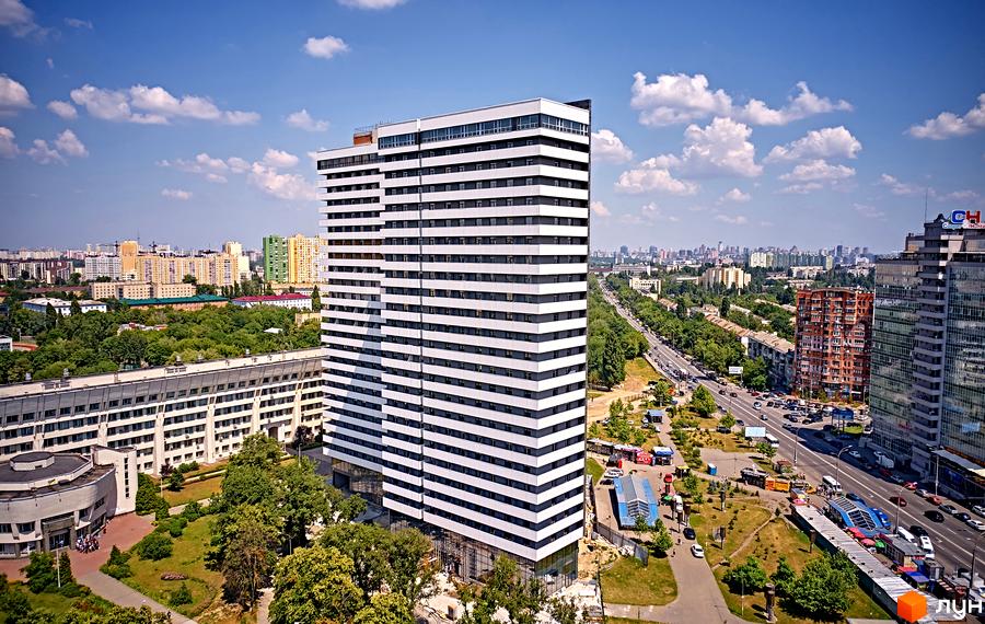 Зображення Житлового комплексу Standard One: висотна будівля з горизонтальними смугами. Навколо зелені насадження та міська інфраструктура.