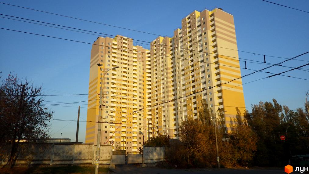 Новобудова на проспекті Науки, 55а. Багатоповерховий житловий комплекс з жовто-бежевими фасадами та балконами. Навколо будинку дерева та елементи міської інфраструктури.