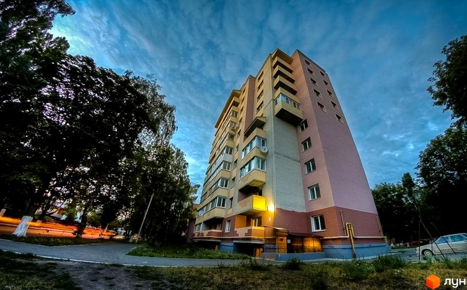 Зовнішній вигляд багатоповерхового будинку на вулиці Вокзальна, 11а. Навколо будинку зелені насадження та доглянута прибудинкова територія.