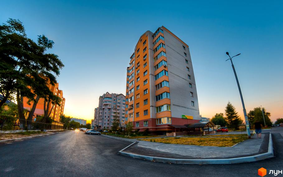 Зовнішній вигляд багатоповерхових будинків на вулиці Вокзальна, 49. Прибудинкова територія з дорогою та зеленими насадженнями.