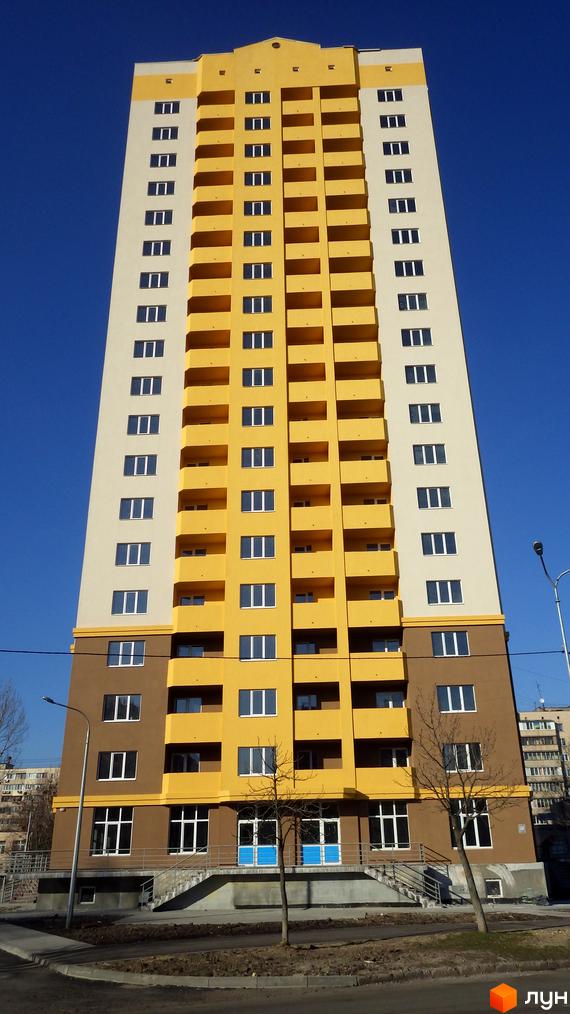 Висотна жовто-біла новобудова з коричневим цоколем на вулиці Булгакова, 13. Будинок має багато балконів та вікон. Перед будинком облаштована прибудинкова територія зі сходами та деревами.