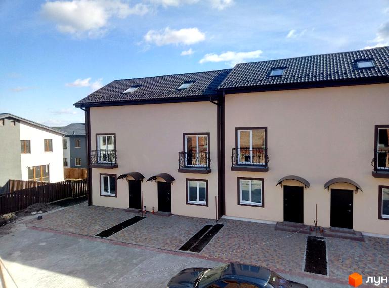 Таунхауси Cherry Town з бежевим фасадом та темним дахом, вікнами з балконами та вхідними групами. Прибудинкова територія з бруківкою та паркомісцями.