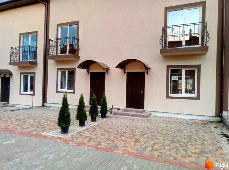 Таунхауси Cherry Town з коричневими дверима та вікнами, балконами з кованими решітками, перед будинком викладений бруківкою двір з туями у горщиках.