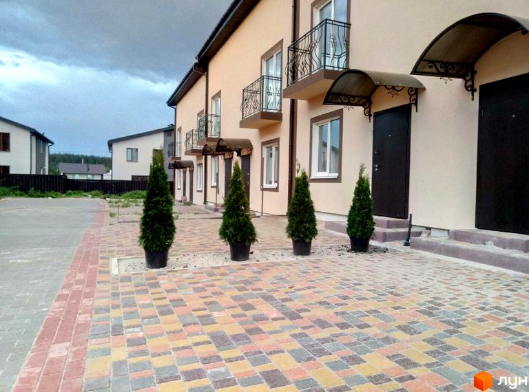 Таунхауси Cherry Town з цегляним фасадом та бруківкою перед будинками. Навколо розташовані зелені туї та сусідні будинки.