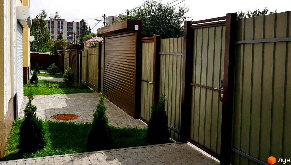 Фасад будинку Котеджного містечка Нова Еллада світлого кольору з коричневими елементами, доглянута прибудинкова територія з бруківкою та зеленню.