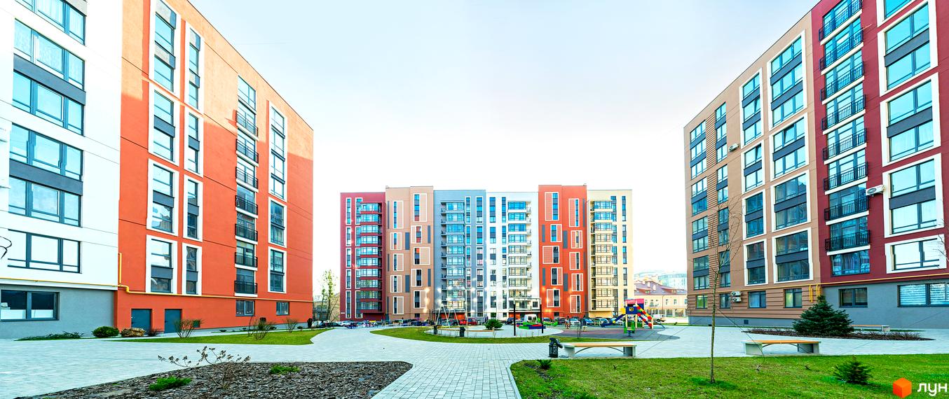 Багатоповерхові будинки житлового комплексу Семицвіт з яскравими фасадами. Поряд з будинками доглянута прибудинкова територія з газонами, доріжками та дитячим майданчиком.