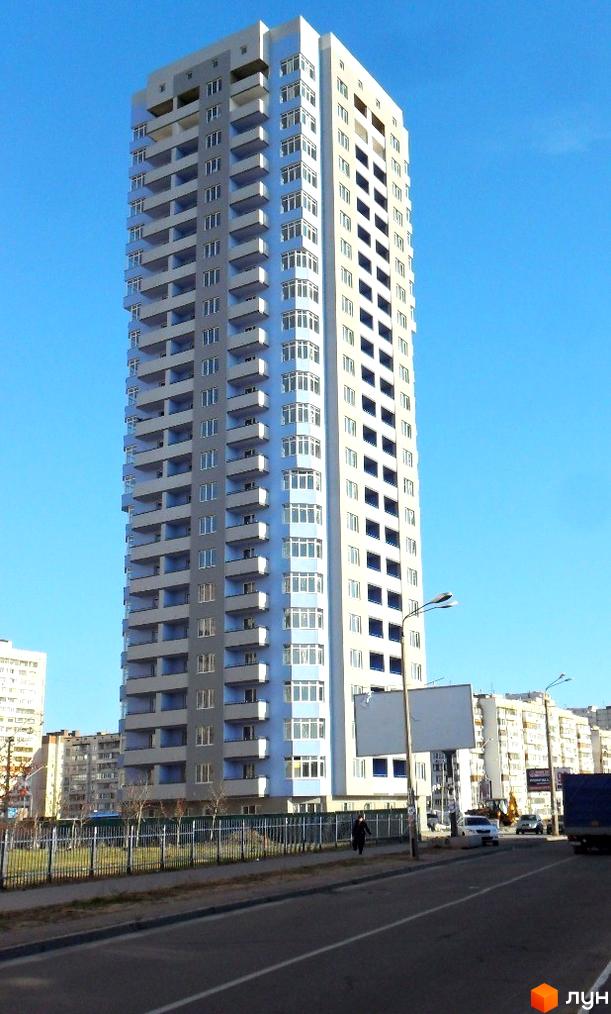 Високоповерховий житловий комплекс на вулиці Гмирі, 17. Будинок має багато балконів та вікон, розташований на фоні блакитного неба. Поруч дорога та паркан.