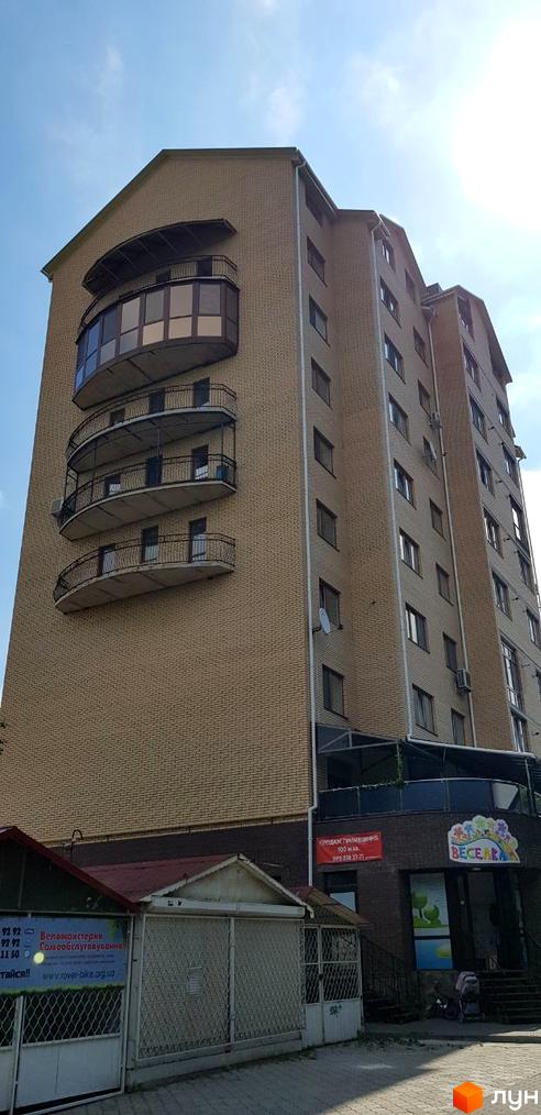 Зовнішній вигляд багатоповерхового будинку з цегляним фасадом та балконами. На першому поверсі розташовані комерційні приміщення та дитячий центр 