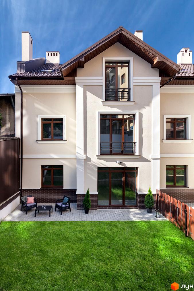 Таунхауси „Вілли на Личаківській“: двоповерховий будинок з коричневим дахом та дерев'яними вікнами, зелена галявина та дерев'яний паркан.