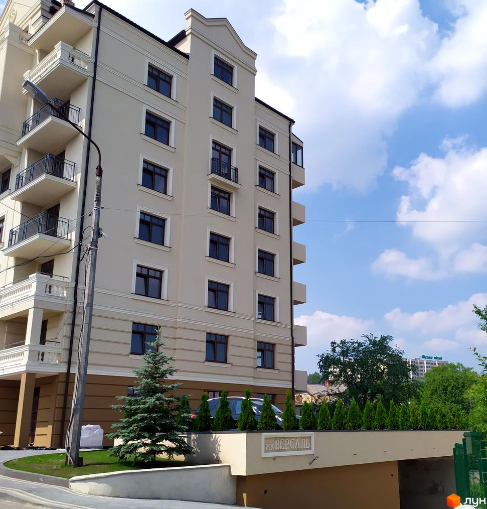 Житловий комплекс Версаль. Багатоповерховий будинок з балконами та великими вікнами. На прибудинковій території висаджені дерева та кущі.