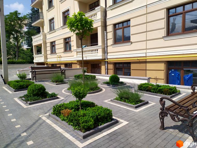 Житловий комплекс Версаль з доглянутою прибудинковою територією. На фото видно будівлю з вікнами та лавки для відпочинку.