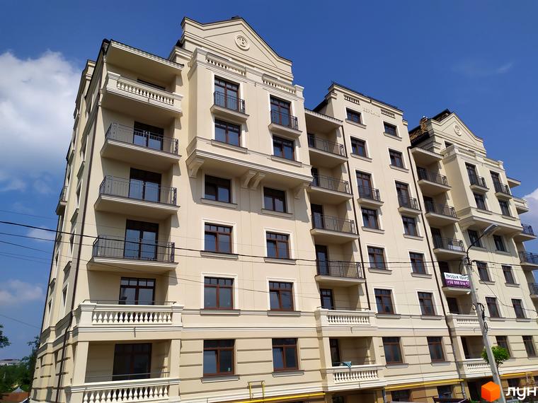 Житловий комплекс Версаль. Багатоквартирний будинок з балконами та світлим фасадом на тлі блакитного неба. На території є зелені насадження та парковка.