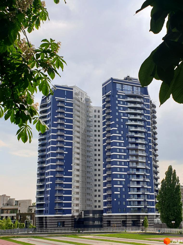 Житловий комплекс Alter Ego - двоколірна висотна будівля з балконами та скляними фасадами. Навколо зелена зона та дерева.