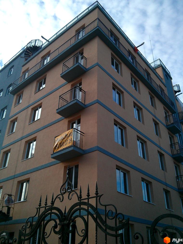 Клубний будинок „Цитадель“ – цегляний будинок з балконами та вікнами, що виходить на вулицю. На фасаді розміщено банер з інформацією про новобудову.