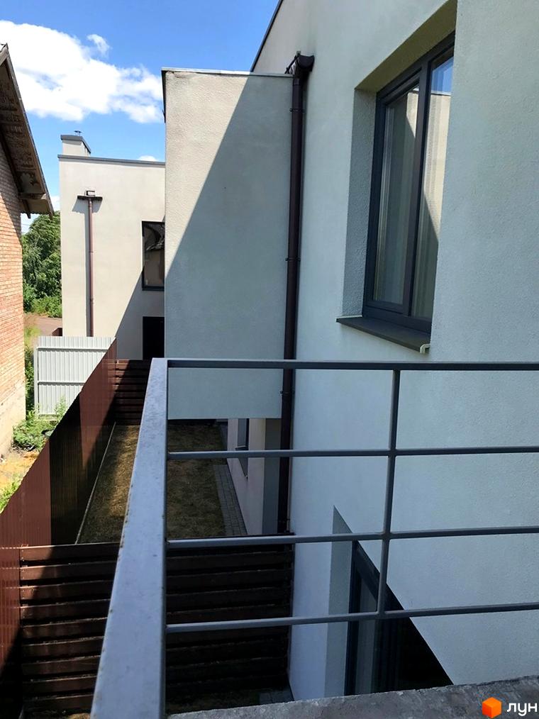 Фасад таунхаусів Monaco з світлими стінами, темними вікнами та балконом. Видно сходи, газон та огорожі на прибудинковій території.