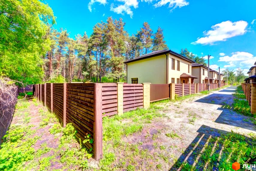 Котеджне містечко Garmonia: ряд двоповерхових будинків світлого кольору з темними дахами. Прибудинкова територія з дерев'яною огорожею та лісом.