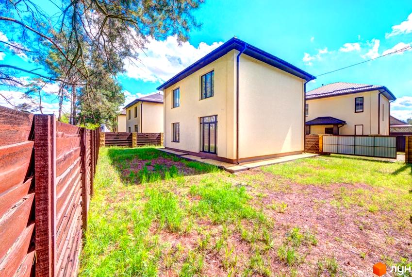 Двоповерховий будинок світлого кольору з темними вікнами та дахом на території Котеджного містечка Garmonia. Прибудинкова ділянка з зеленим газоном та дерев'яним парканом.