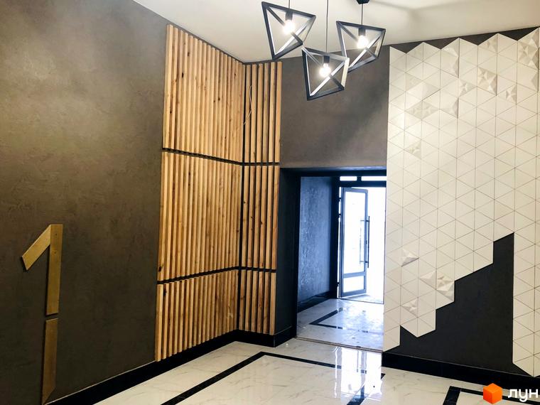 Інтер'єр холу новобудови ЖК Перлина Проскурова з дерев'яними панелями та геометричним декором на стіні. На стіні видно цифру 1.