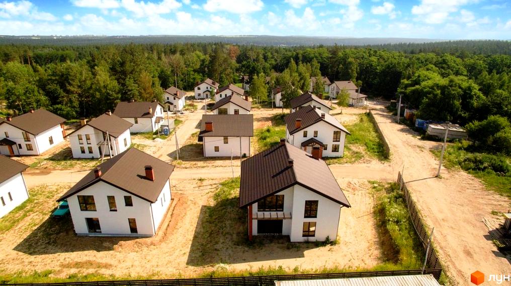 Котеджне містечко Ліс та Озеро. Білі будинки з коричневими дахами розташовані серед зелених дерев та піщаної дороги.