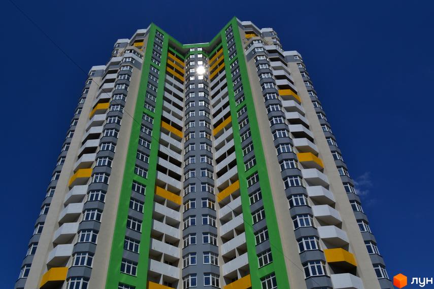 Багатоповерховий житловий комплекс Паркова Вежа з яскравим фасадом у зелених та жовтих кольорах. Будинок має багато балконів та вікон, розташований на фоні синього неба.