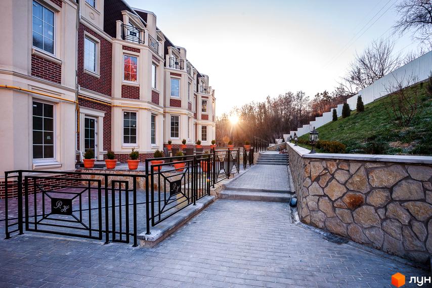 Таунхауси Royal Hill з цегляним фасадом та елегантною прибудинковою територією з бруківки та кам'яної кладки. Сонячний захід сонця над комплексом.