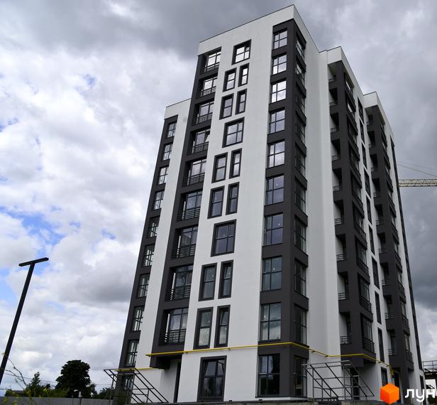 Новобудова ЖК Супернова з біло-сірими фасадами та великою кількістю вікон. Будинок має багатоповерхову структуру з балконами. Навколо будівлі видно елементи будівельних робіт та зелені насадження.