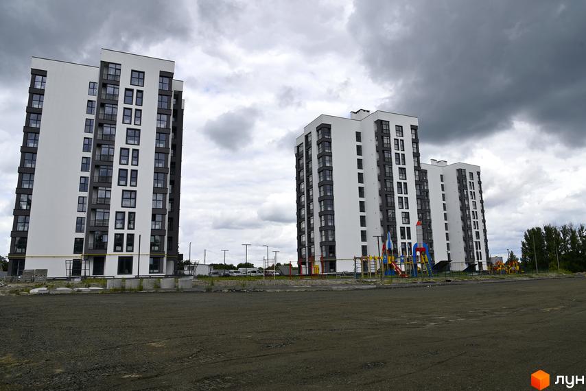 Житловий комплекс Супернова. Сучасні білі багатоповерхові будинки з темними віконними рамами та балконами. Поруч дитячий майданчик з гірками та гойдалками.