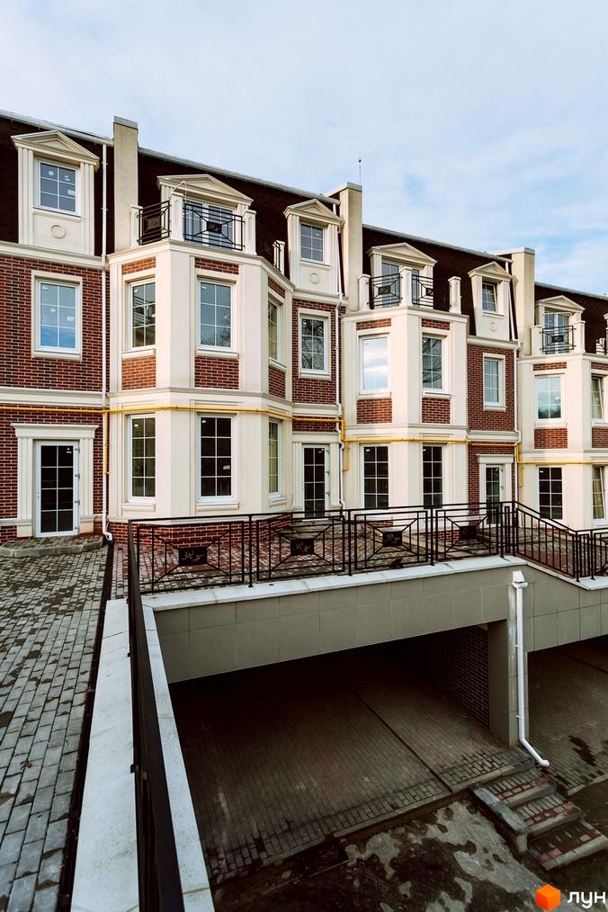 Таунхауси Royal Hill з цегляним фасадом та білими елементами. Прибудинкова територія з бруківкою та огороженим входом до паркінгу.