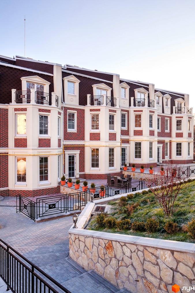 Таунхауси Royal Hill з цегляним фасадом та мансардним дахом. Навколо облаштована територія з брукованими доріжками та кам'яною стіною.