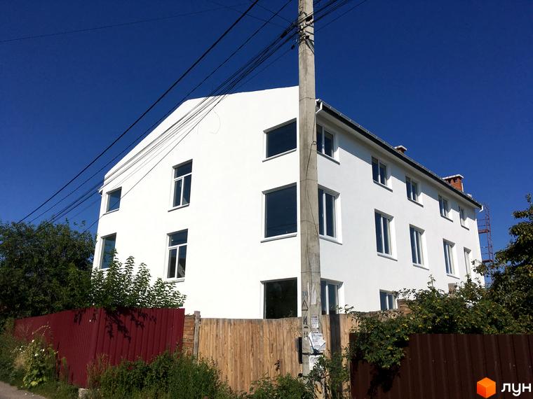 Біла триповерхова новобудова Женева з великими вікнами, оточена зеленими насадженнями та парканом.