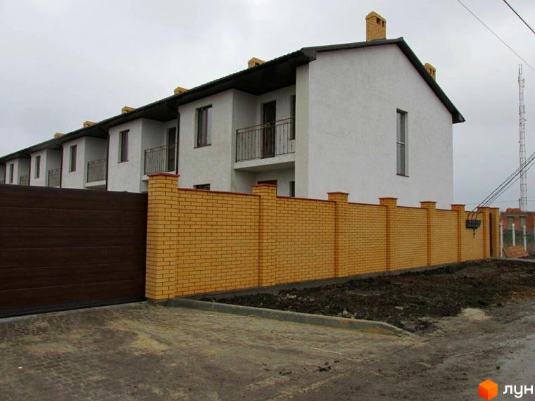 Житловий комплекс з цегляним парканом та автоматичними воротами. На території комплексу висаджено дерева та кущі, є доріжки.