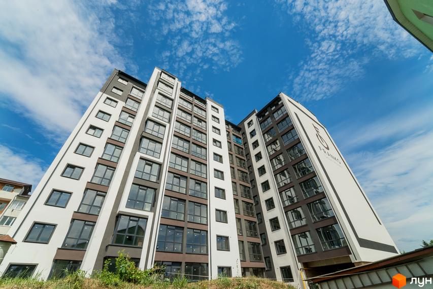 Висотна будівля ЖК Franko Smart House з великою кількістю вікон на фоні блакитного неба. Поруч з будинком видно зелень та прибудинкова територія.