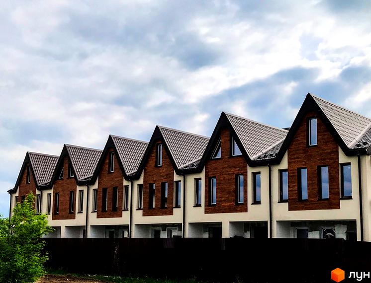 Зображення таунхаусів New Smart 2 з коричневими дахами та фасадами, розташованих за коричневим парканом на тлі хмарного неба.