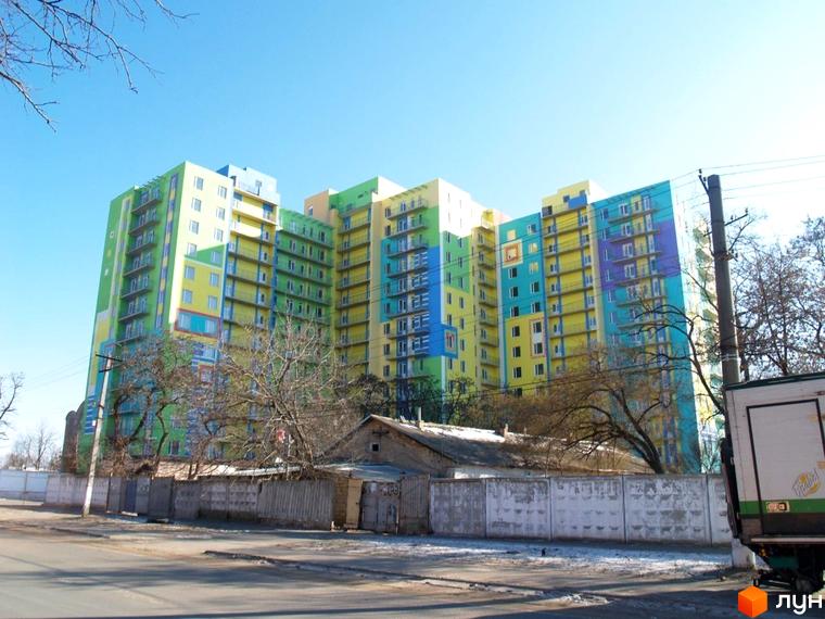 Багатоповерховий Житловий комплекс Іспанський з яскравими жовтими, зеленими та синіми фасадами. На передньому плані видно дорогу, огорожу та дерева без листя.