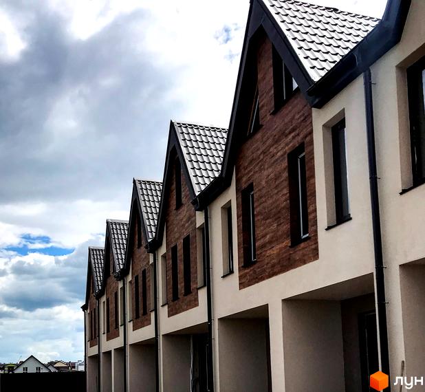 Зображення фасаду таунхаусів New Smart 2 з коричневим оздобленням стін та темною покрівлею. Видно ряд будинків з великими вікнами на фоні хмарного неба.