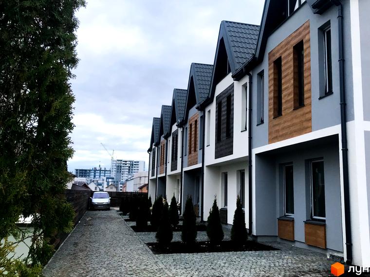 Зовнішній вигляд таунхаусів New Smart 1 з сірим та дерев'яним фасадом. Прибудинкова територія з вимощеною доріжкою та туями.