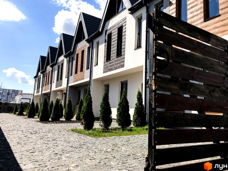 Зовнішній вигляд таунхаусів New Smart 1 з дерев'яним фасадом та бруківкою на прибудинковій території. Комплекс з акуратними туями та парканом.